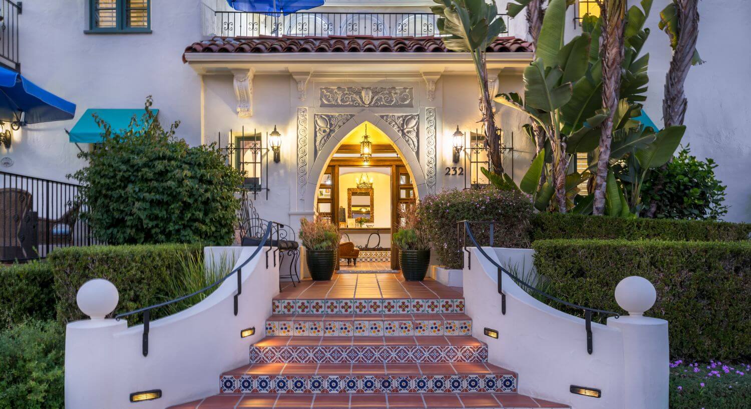 steps in between foliage leading into the building through a diamond shaped doorway, balcony on 2nd floor