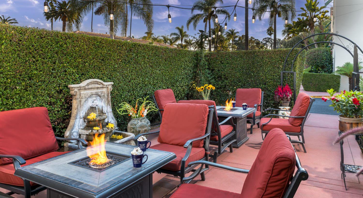 shrub enclosed patio with multiple fire pits with red cushioned seats, fountain, potted plants