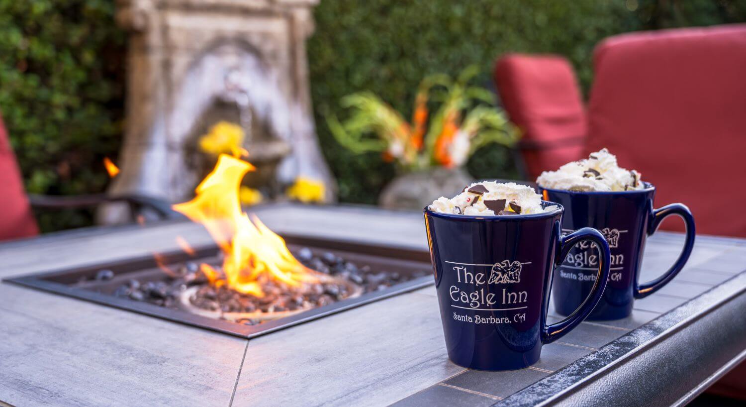 two mugs of hot chocolate with The Eagle Inn logo sitting on edge by fire pit