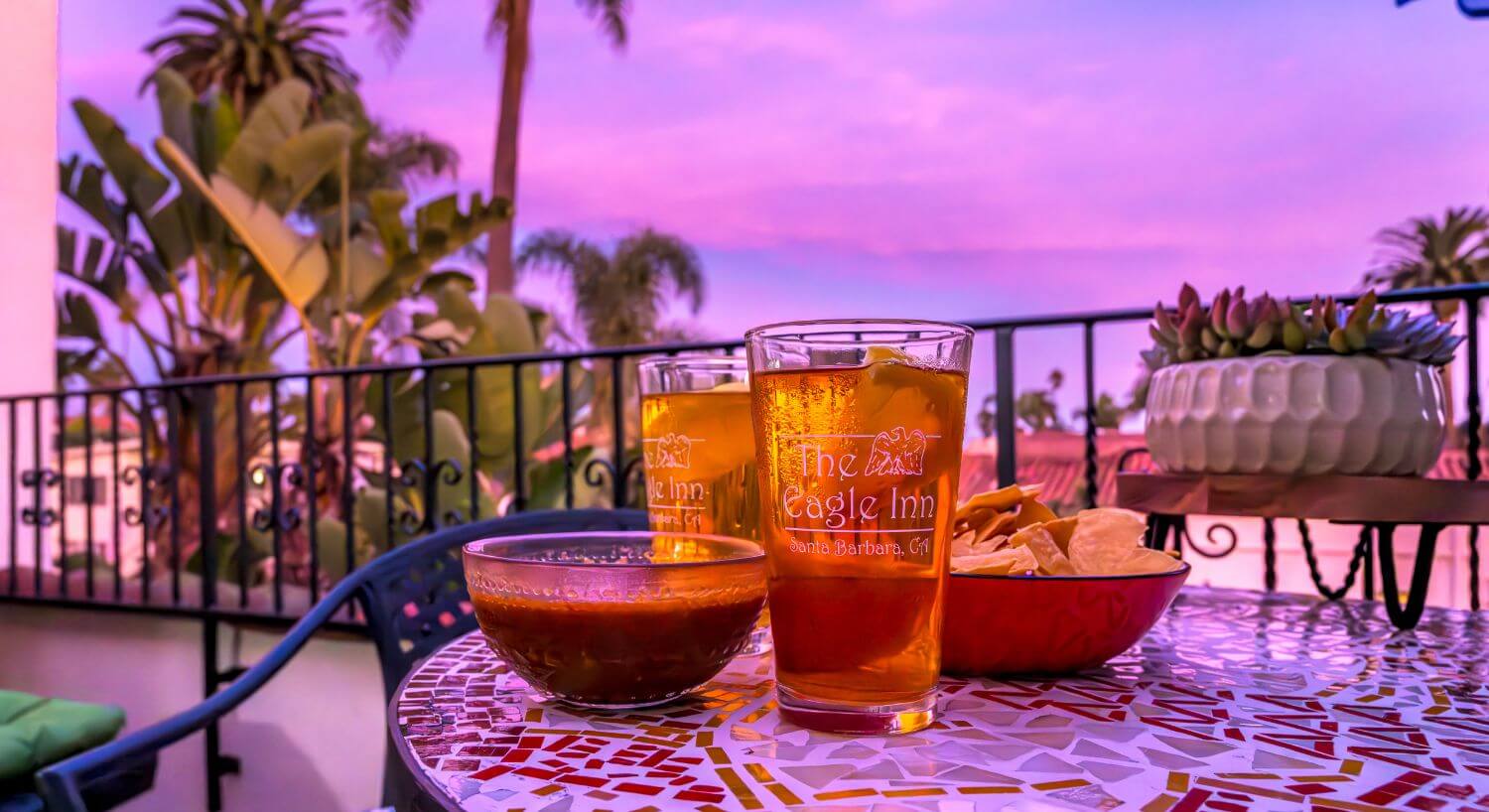 two glasses with the eagle inn logo filled with iced tea, chips and salsa in bowls sitting on table at dusk