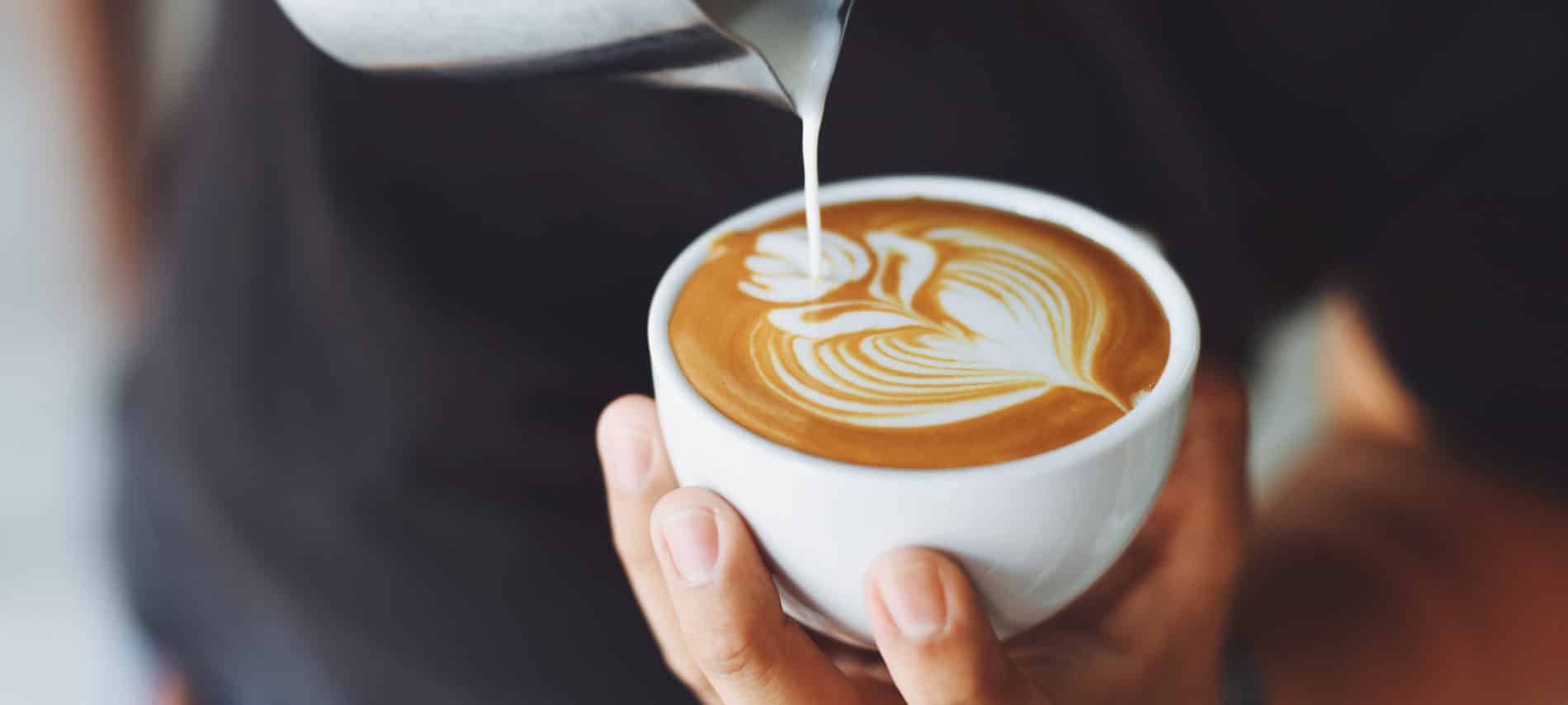 Person pouring milk into a cappuccino