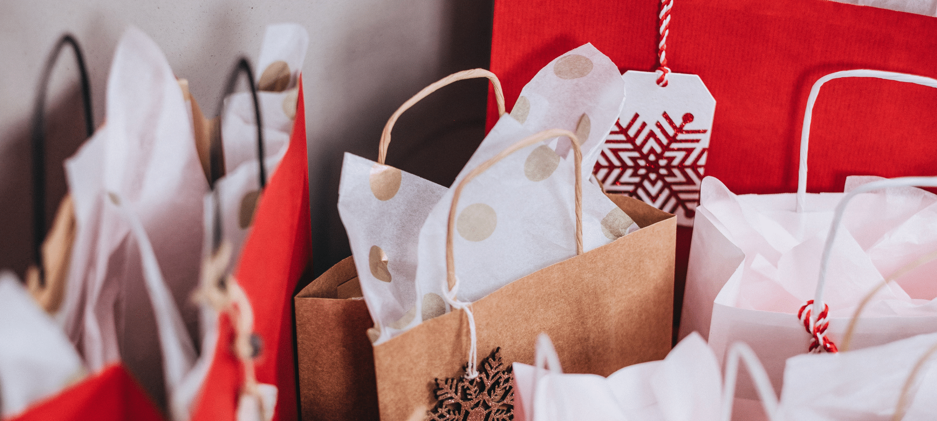 holiday gift bags filled with tissue paper and festive tags arranged closely together