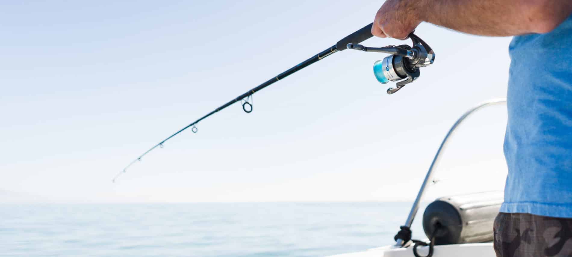 blue sky, darker blue water and hands holding a fishing pole over the side of the boat.
