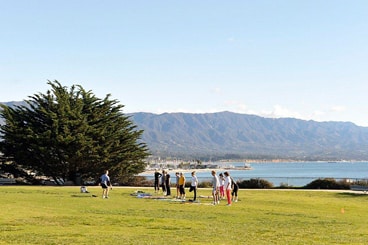 green lawn by water, blue sky, group of people in distance taking an exercise calss