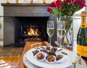 Silver tray on a round table topped with chilled champagne, two full champagne flutes and three tiered tray with goodies