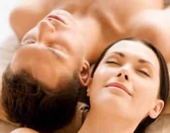 Man and woman laying head to head on table during couples massage