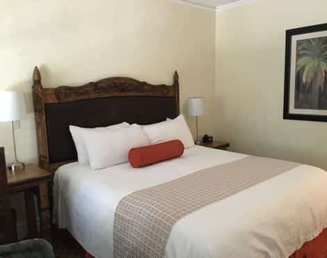 Guest room with ivory wall, wood and leather headboard, white bedding and nightstand with lamp