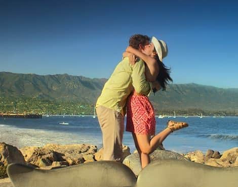 Man and woman embracing on the beach with ocean and mountains in the background