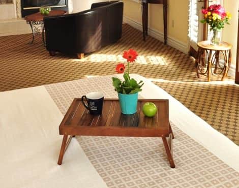 Guest bed topped with a wooden tray with red flowers, a green apple and black mug