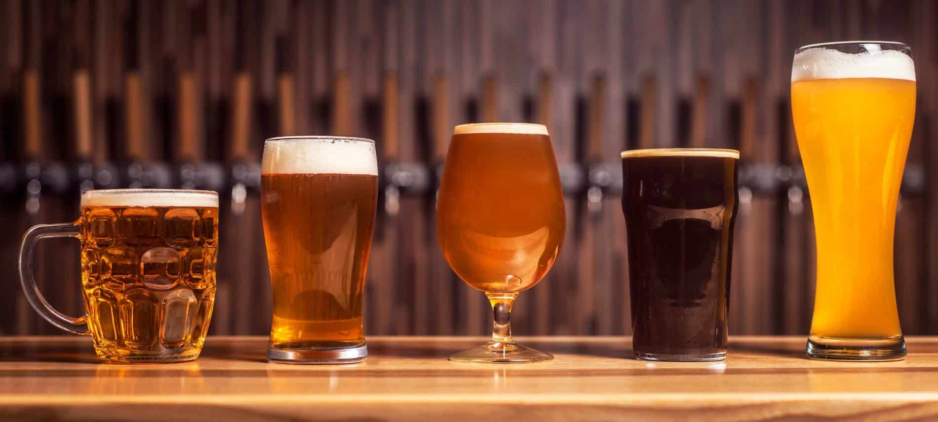 Five different craft beers in unique glasses lined up on a bar counter