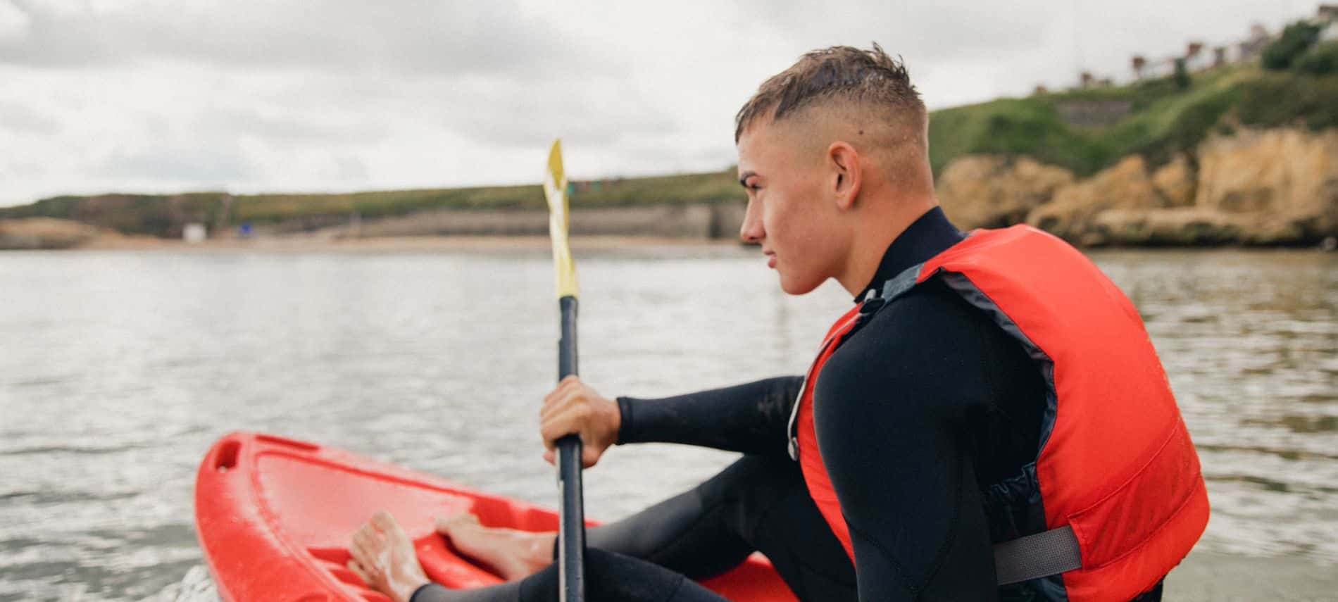 A boy kayaking around a bay in a red kayak with the beach in the background