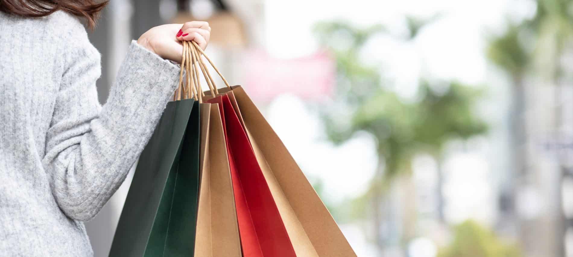 A woman in a grey sweater holds red, green, and brown shopping bags