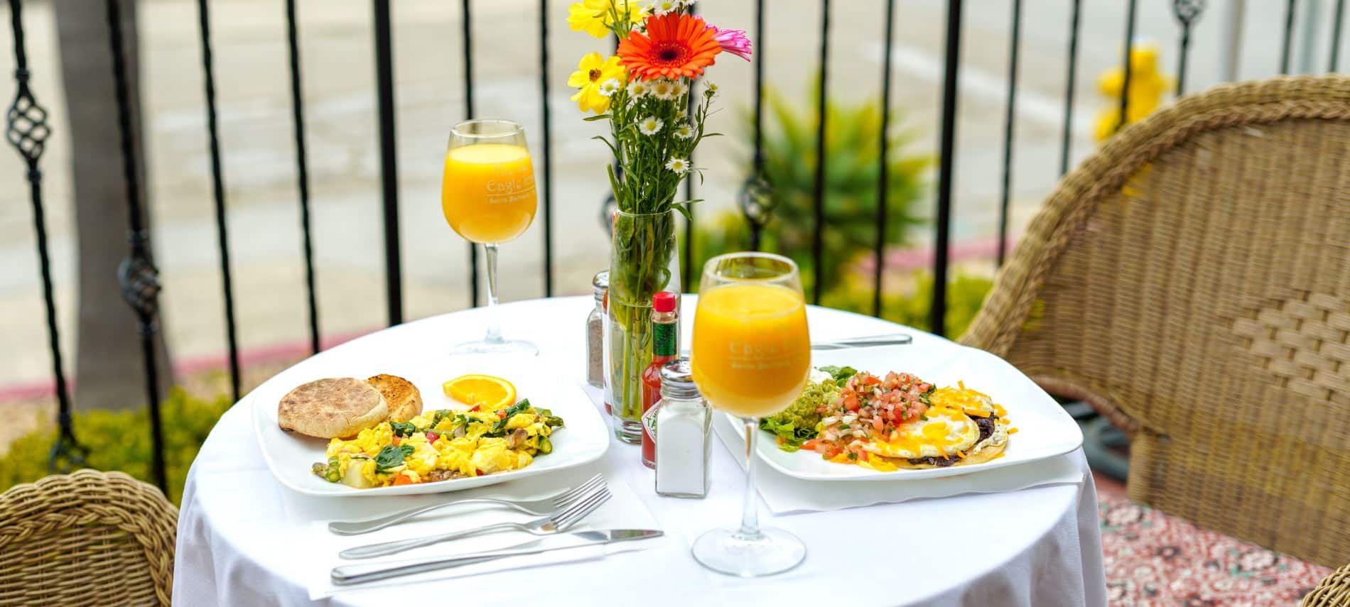 Two plates of breakfast with goblets of orange juice laid out on a table with a white tablecloth on the patio at The Eagle Inn