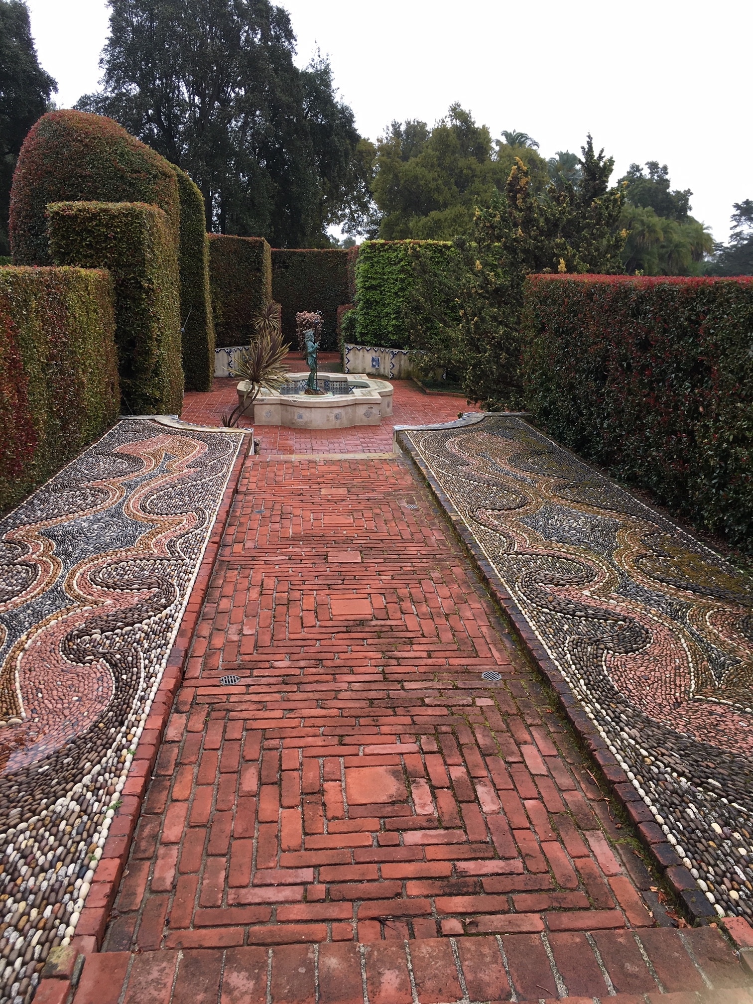 Brick mosaic path lined by formally manicured shrubs