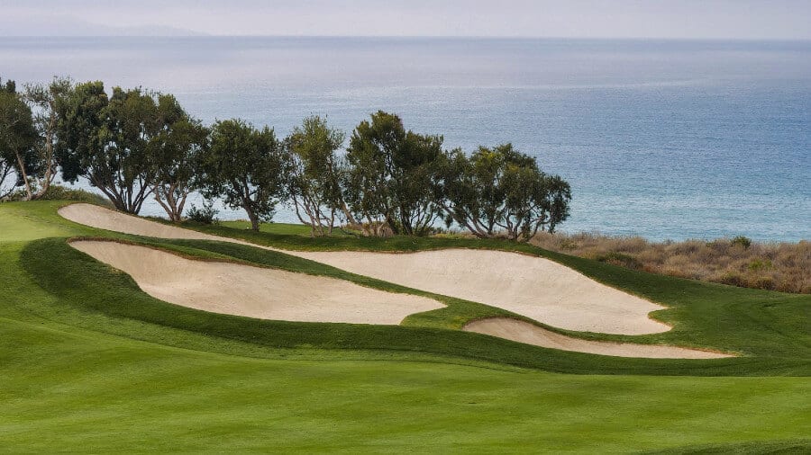 golf course with large sandtraps position along ocean with trees in between