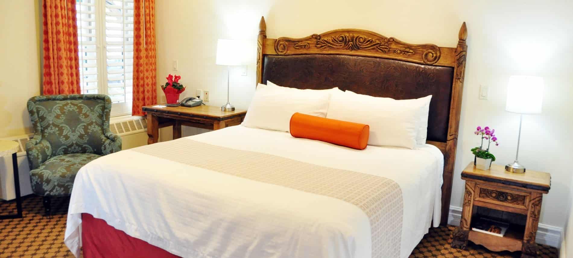 Guest room with ivory walls, wood and leather headboard, nightstand with lamps and upholstered chair