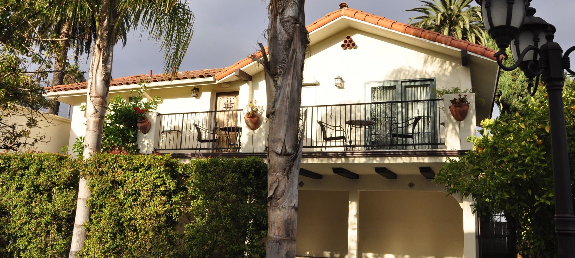 Exterior view of casitas with ivory stucco, red tile roof, balcony with metal railing, green shrubs and palm trees