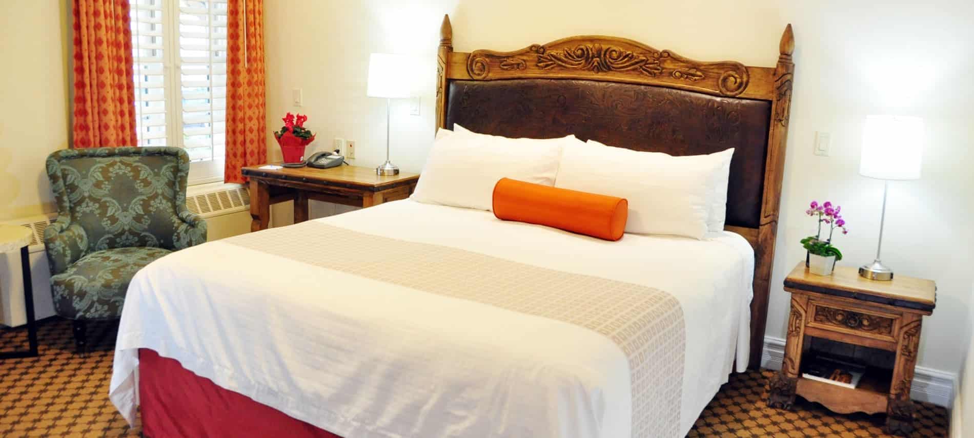 Guest room with ivory walls, wood and leather headboard, nightstand with lamps and upholstered chair