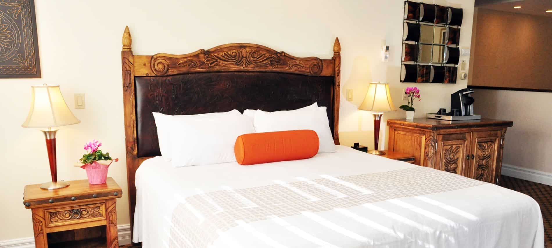 Guest room with ivory walls, wood and leather headboard, nightstands with lamps and side table with coffee maker