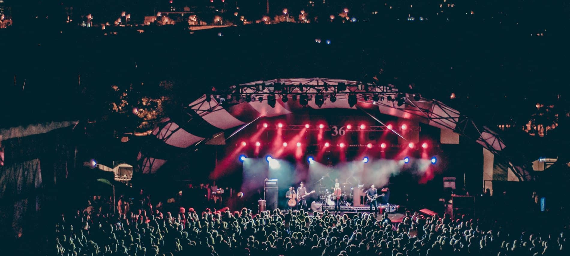 Concert venue packed with fans, band on stage with red spotlights