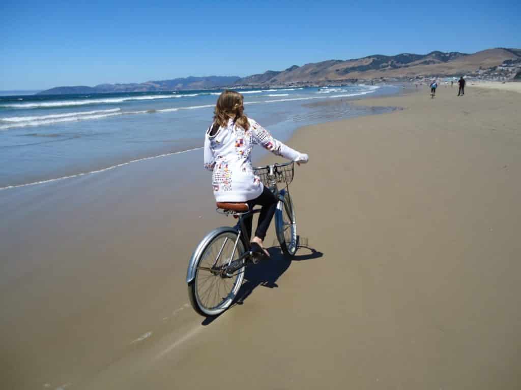 Woman riding her bike on hard-packed sand along the Pacific Ocean