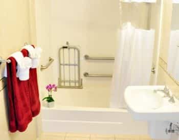 Guest bath with ivory walls, white tub and pedestal sink and red and white towels