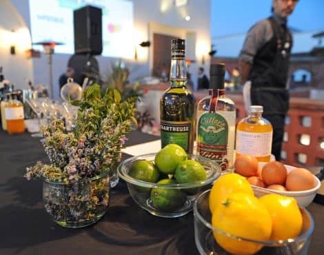 Table topped with bowls of limes, lemons and eggs, and fresh herbs and bottles nearby