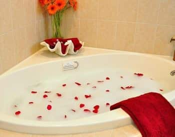 White corner tub with tile surround filled with bubbles and red rose petals