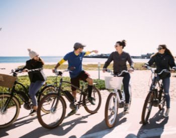 Group of 4 individuals on path sitting on ebike. View of ocean behind the group.