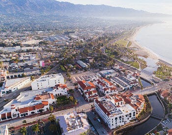 aerial view of homes and buildings with ocean on right and mountains in background