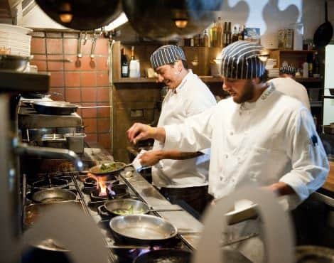 Chefs in white coats and striped hats cooking over a stove in the kitchen