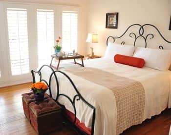 Santa Barbara guest room with scrolled metal bed, white bedding, nightstand with lamp and fresh flowers