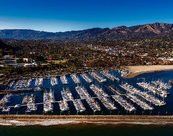 santa barbara harbor with boats anchored with homes and mountains in distance