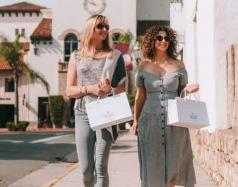 Two women walking down a street in Santa Barbara carrying shopping bags