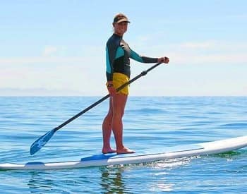 Woman standing on a paddle board carrying an oar and smiling