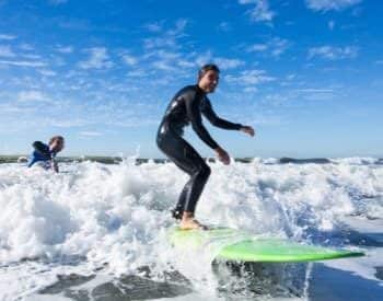 Man in wetsuit on green surfboard riding the waves with another man in water behind