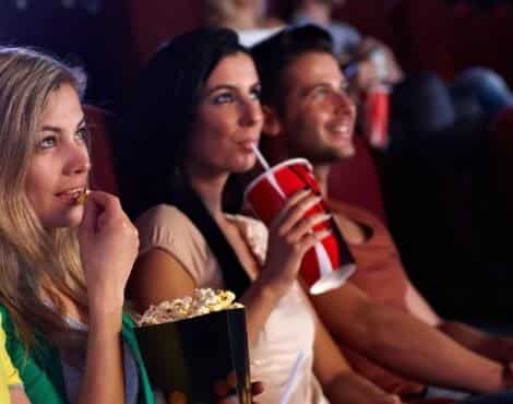 Three people looking up at a theater screen while sipping drinks and eating popcorn