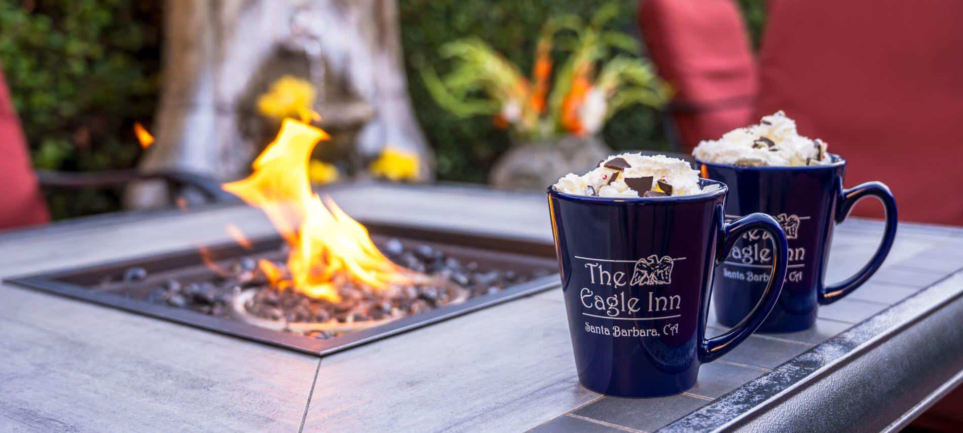 two mugs of hot chocolate with The Eagle Inn logo sitting on edge by fire pit