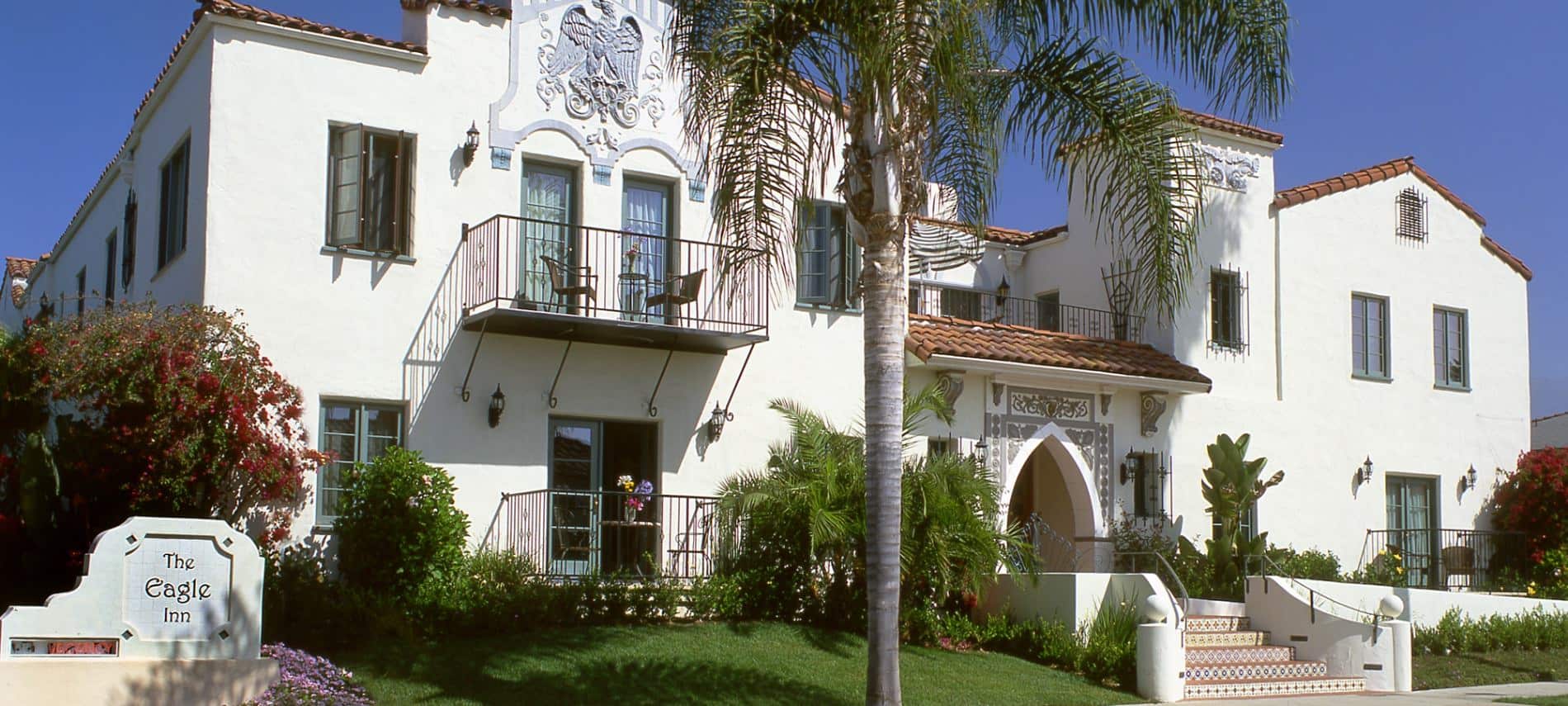 Exterior view of Spanish-style Eagle Inn with palm trees and blue skies