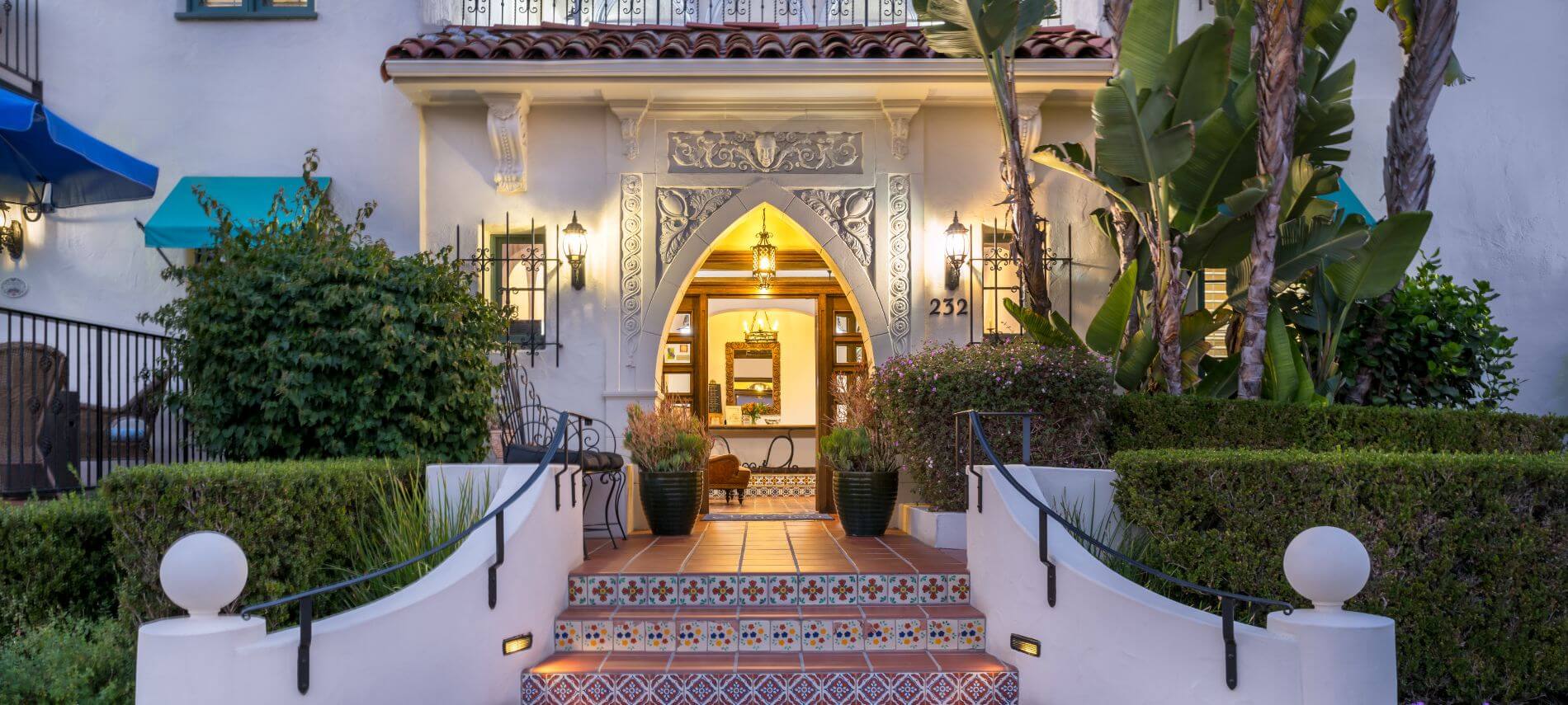 steps in between foliage leading into the building through a diamond shaped doorway, balcony on 2nd floor