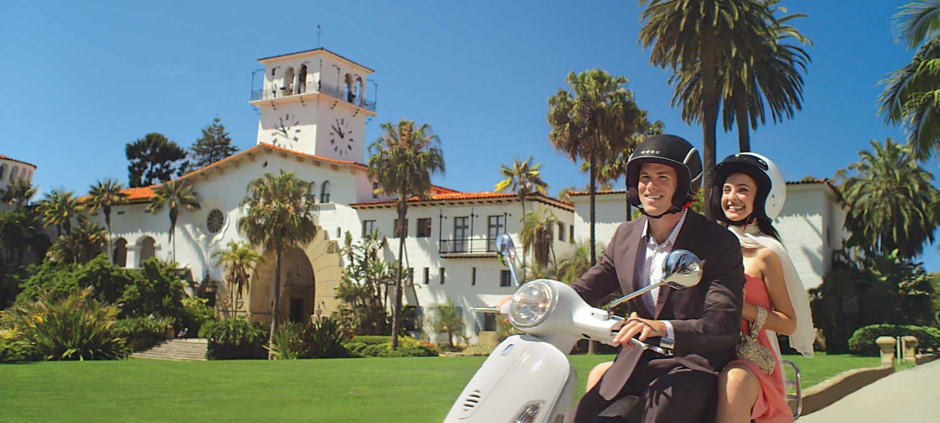 Bride and groom on white mope riding down the street amidst palm trees and blue skies