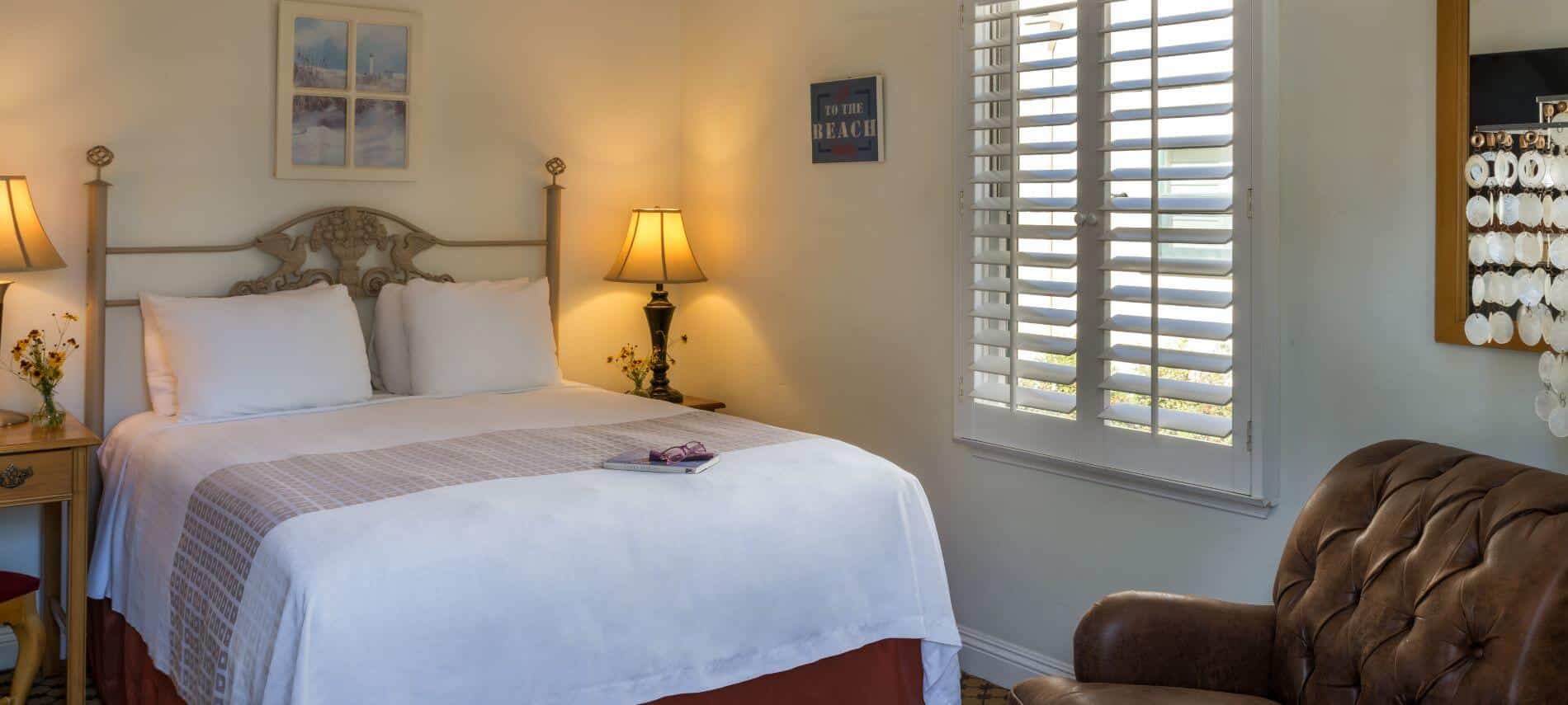 well lit room with queen bed, brown chair, stands with lamps