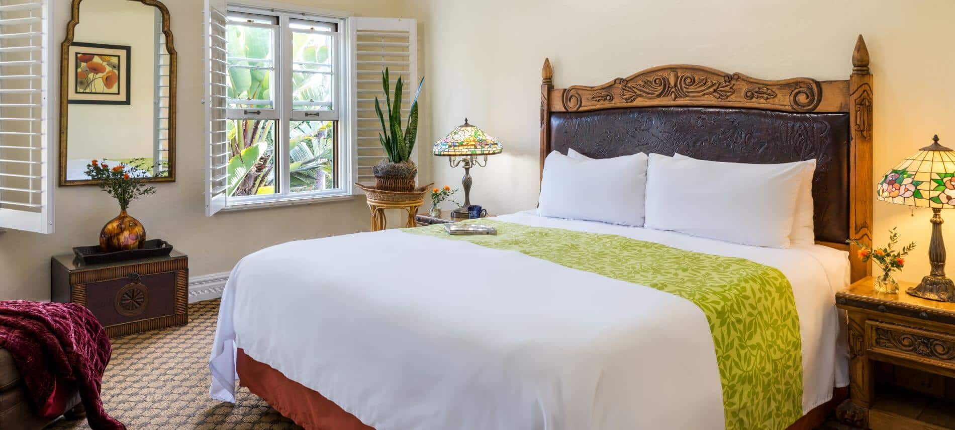 tan carpeted room with king bed with ornate headboard, stands by bed with tiffany style lamps, gold framed mirror on wall