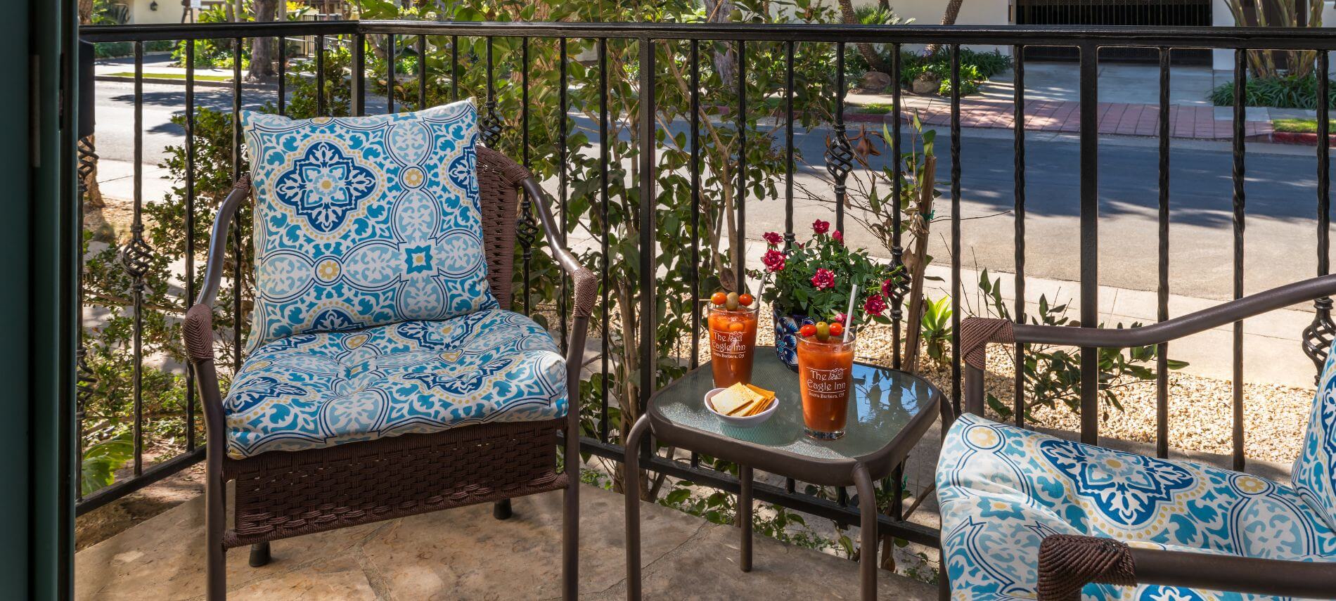 private patio with small table holding refreshments and flowers, wicker blue cushioned chairs