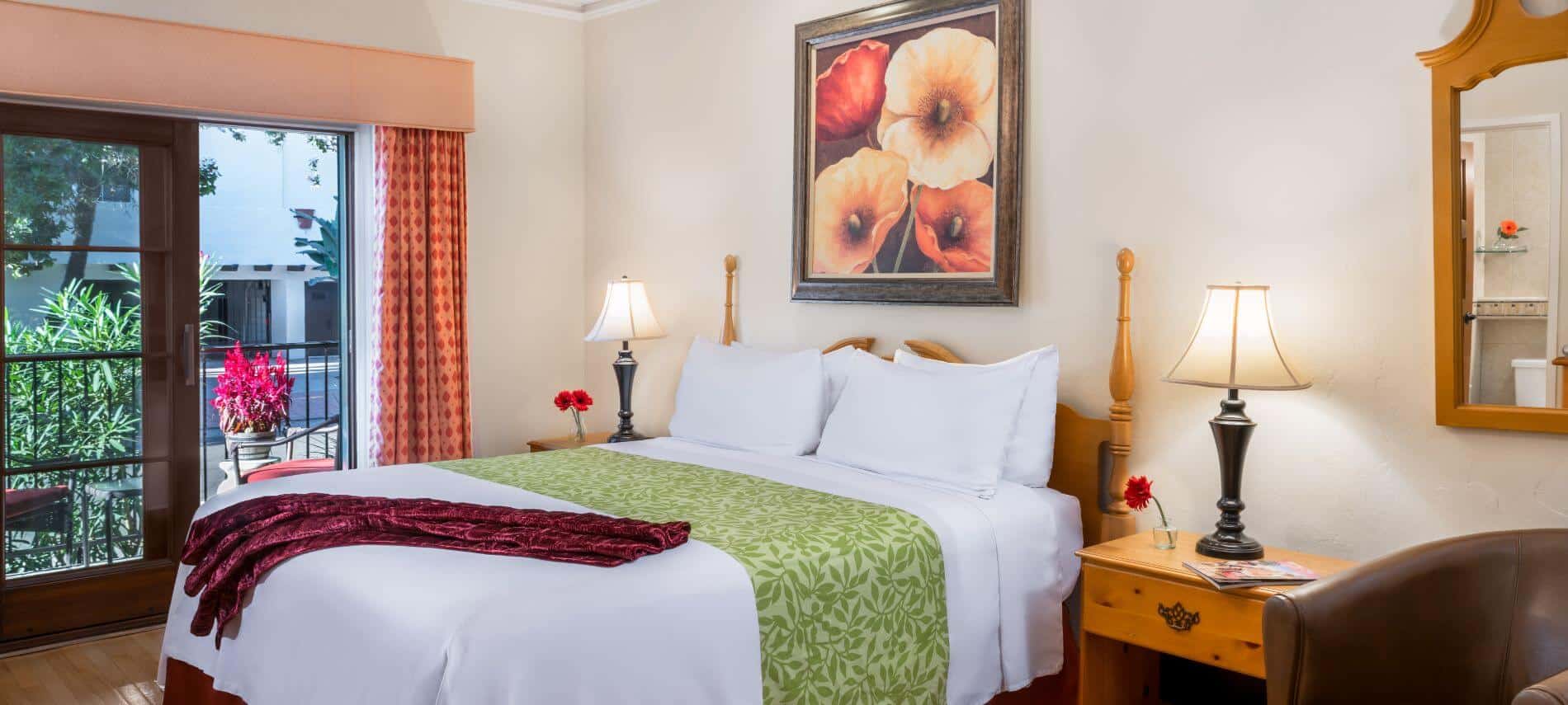 well lit 1st level cream room with stands with lamps, flowers in vases, walk out patio, mirror on wall over brown chair