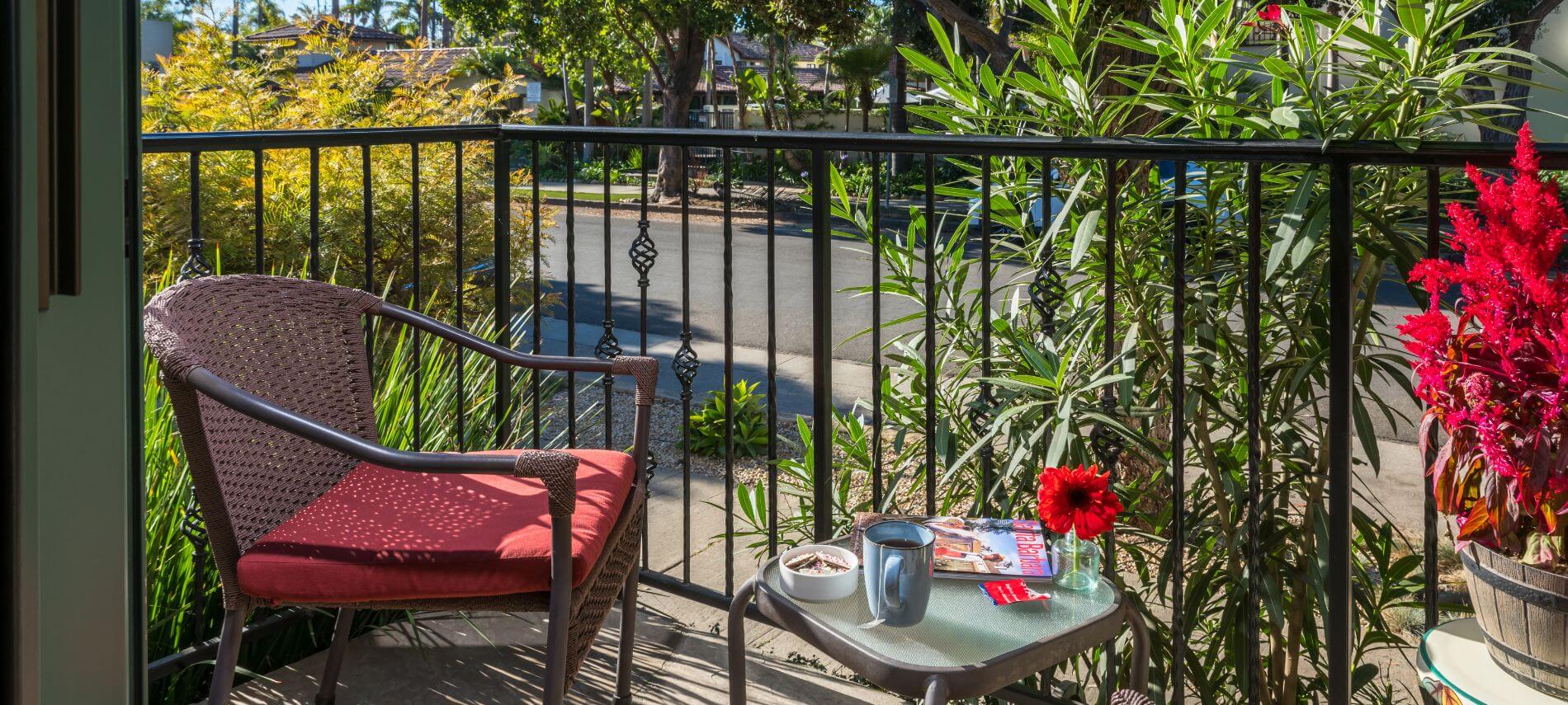 enclosed patio with brown wicker red cushioned chair, small table with magazine and coffee cup, flower in vase
