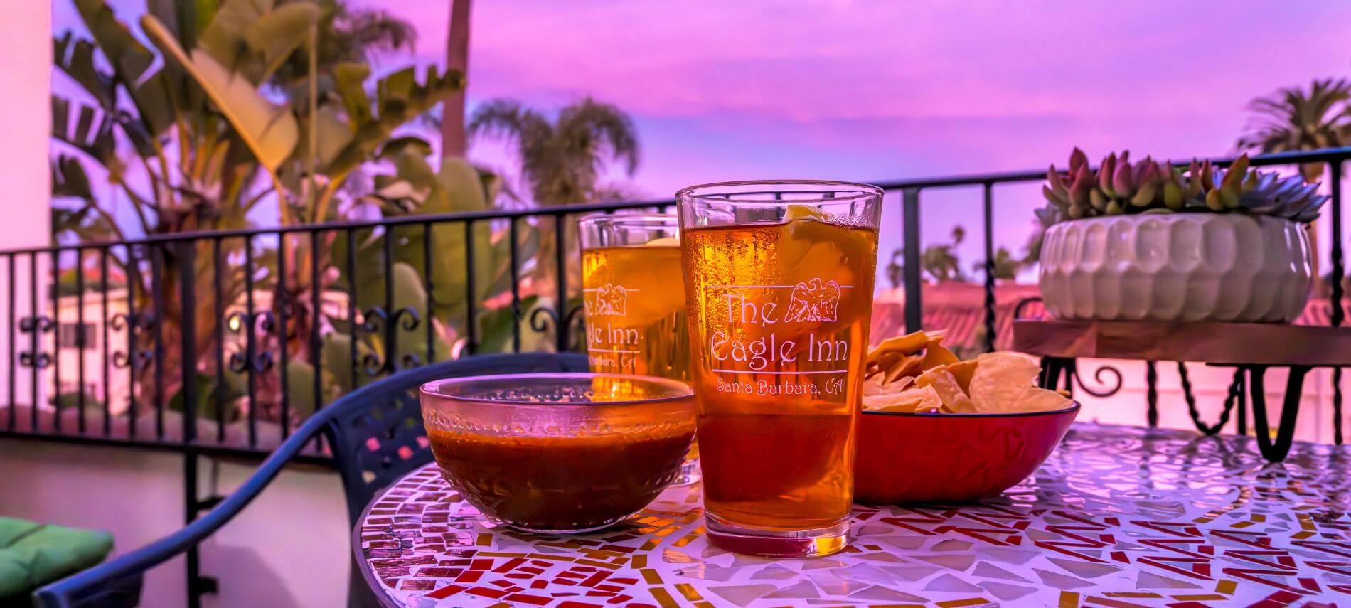 two glasses with the eagle inn logo filled with iced tea, chips and salsa in bowls sitting on table at dusk