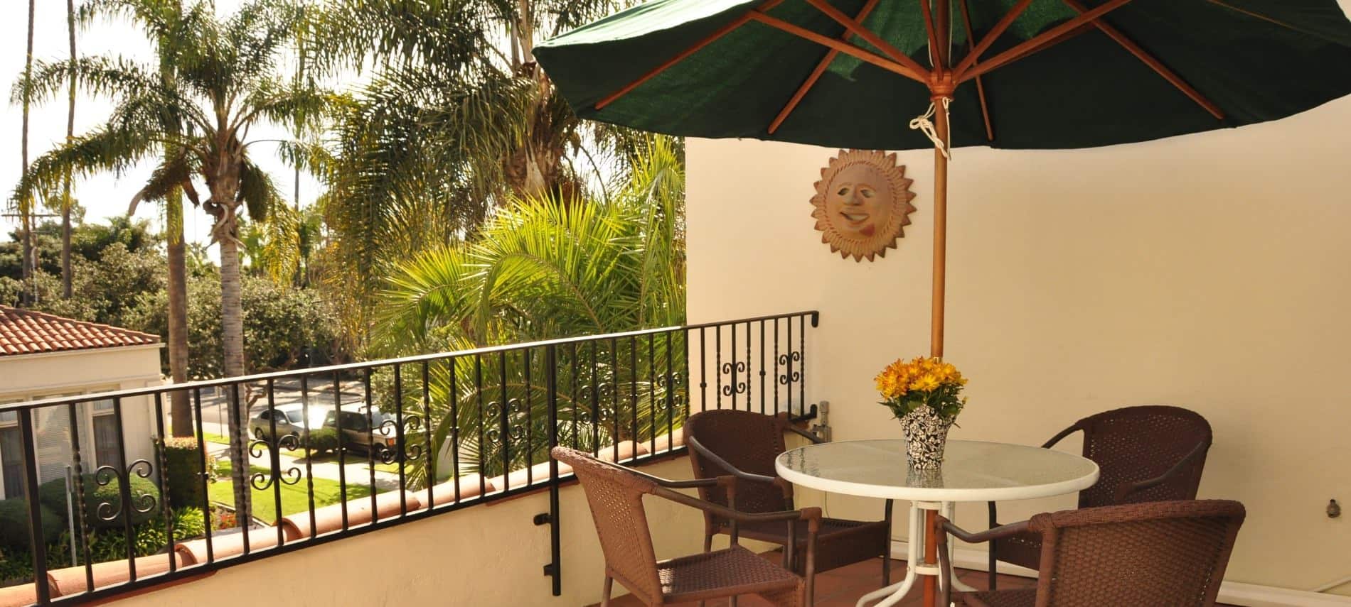 Balcony from a Queen guest room with patio table, chairs, and umbrella overlooking palm trees