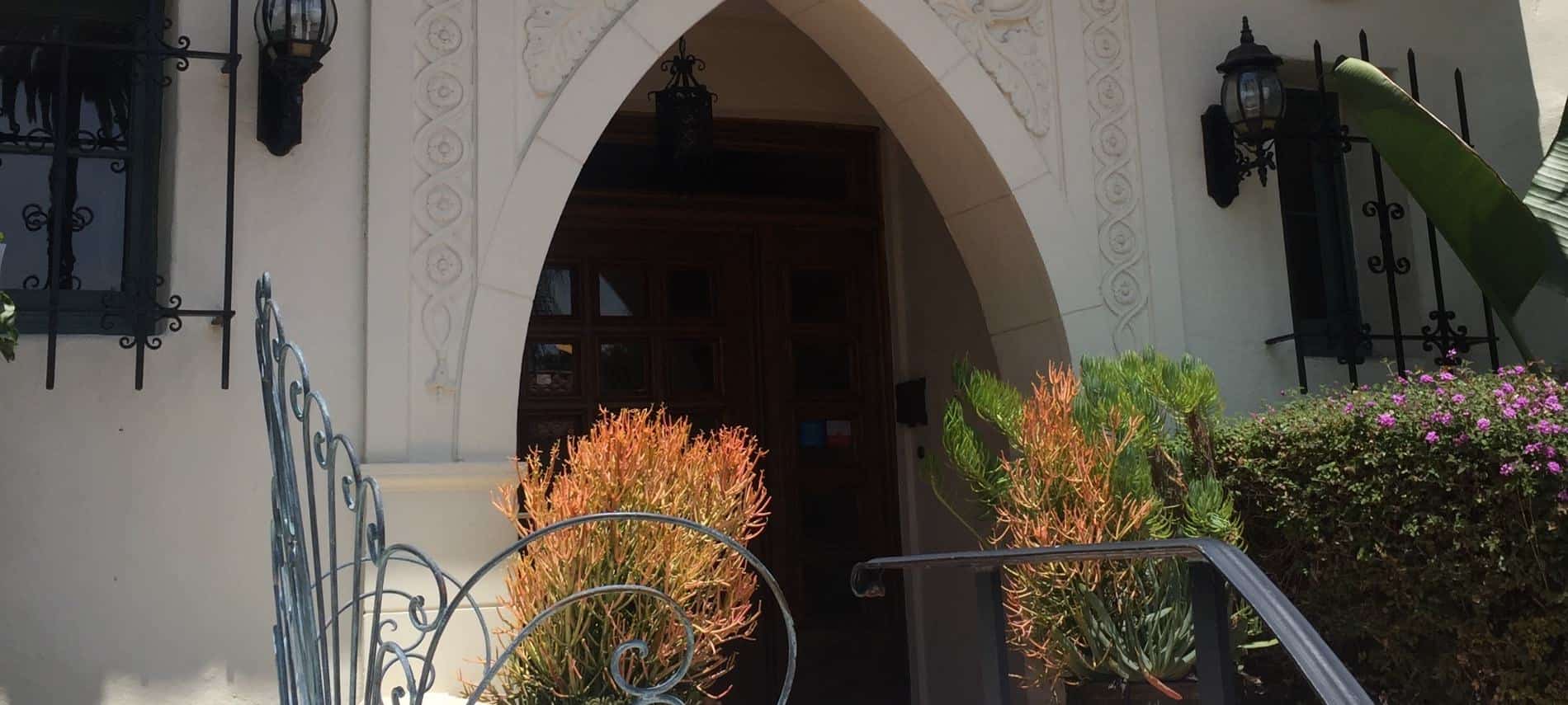 Front entrance to building surrounded by green shrubs with purple flowers and metal railing