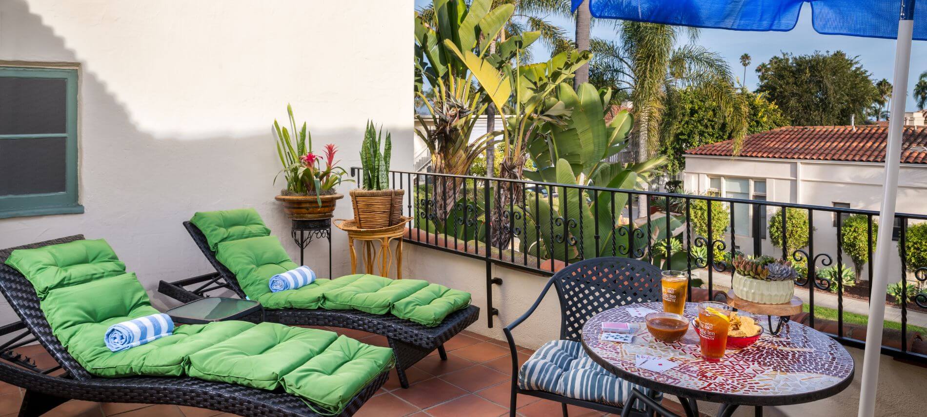 private patio with green cushioned lawn chairs, round table with metal cushioned chairs under blue umbrella